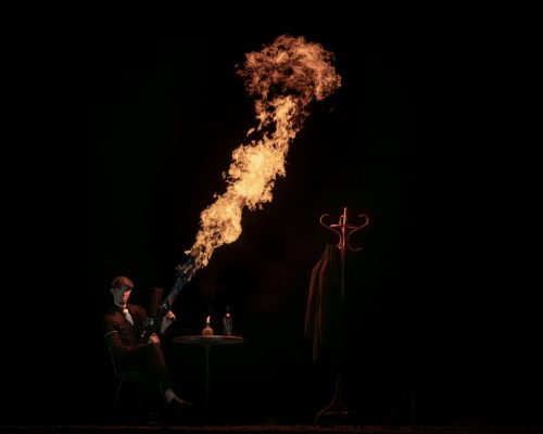 Un artiste habillé en Peaky Blinders est assis à une table et déclenche un lance-flamme qu'il a entre les mains