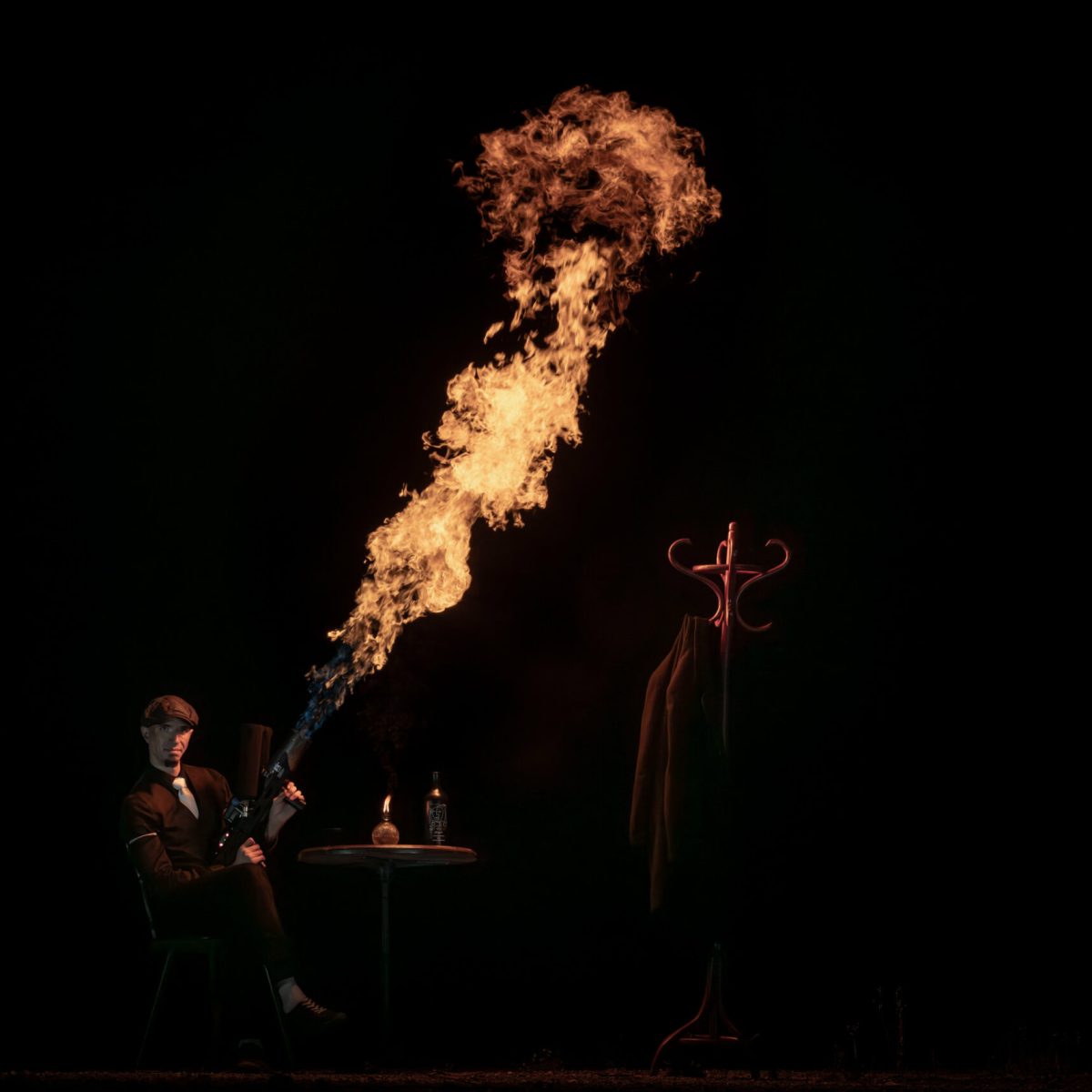 Un artiste habillé en Peaky Blinders est assis à une table et déclenche un lance-flamme qu'il a entre les mains