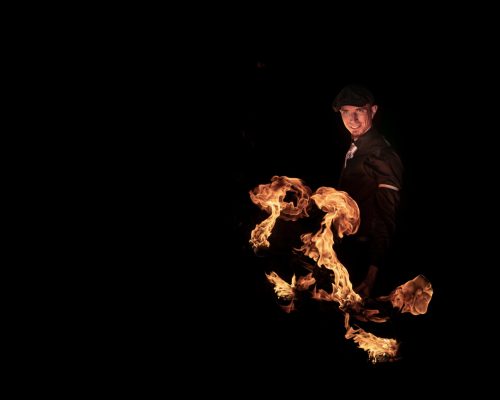 Un artiste habillé en Peaky Blinders avec un dragonstaff en feu et des flammes qui montent
