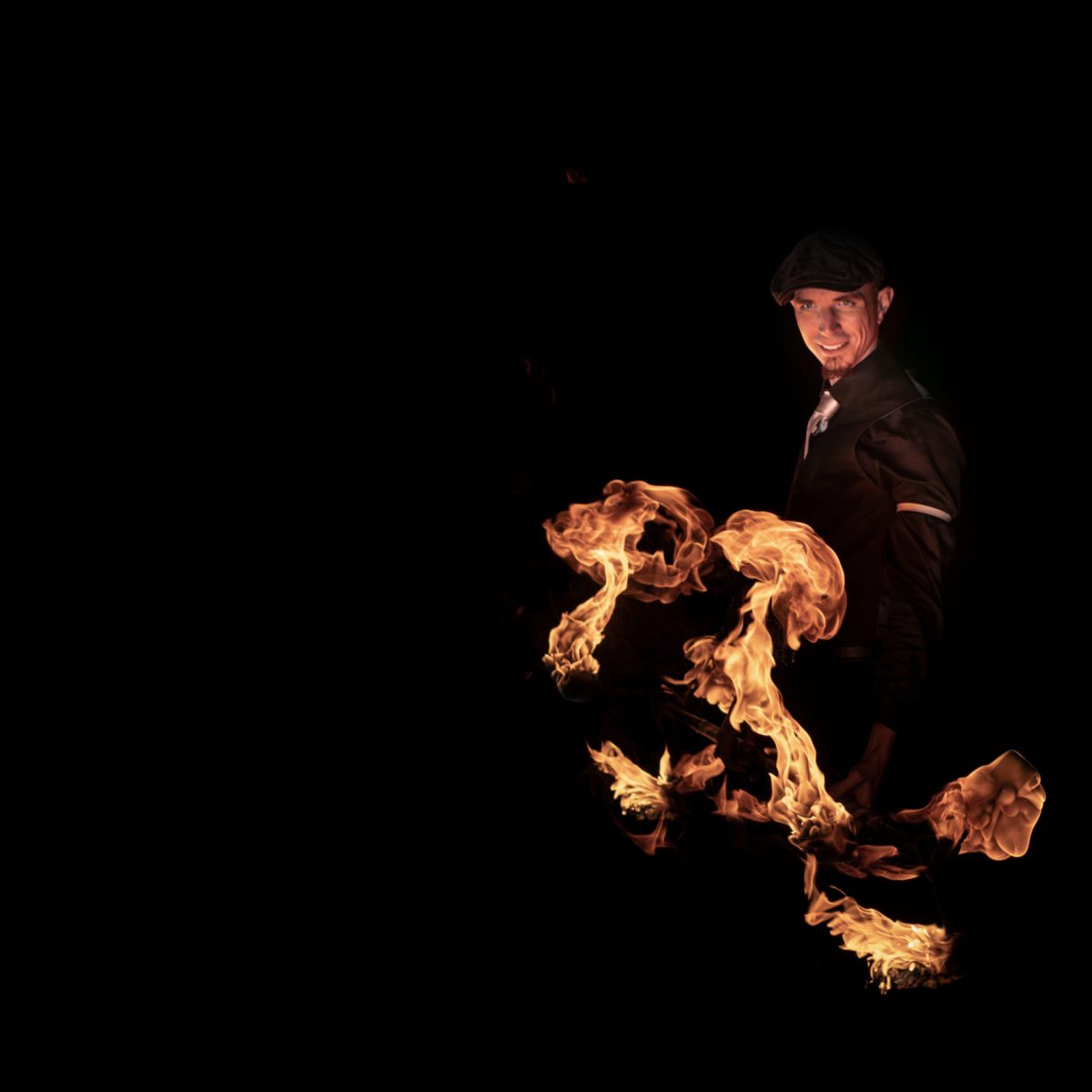 Un artiste habillé en Peaky Blinders avec un dragonstaff en feu et des flammes qui montent