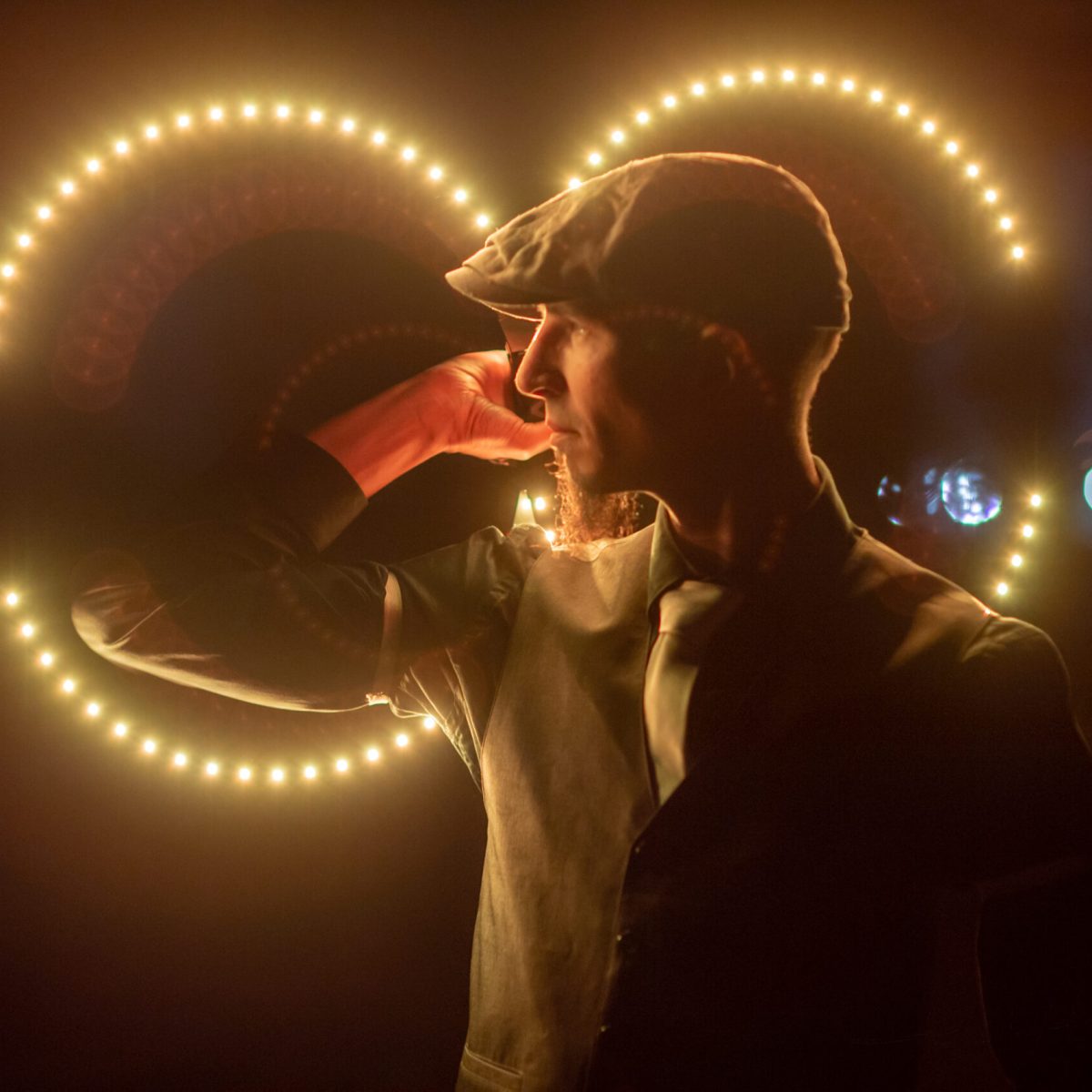 Un artiste de profil et bien habillé avec des buugeng LED (lumineux) derrière lui qui l'illuminent.