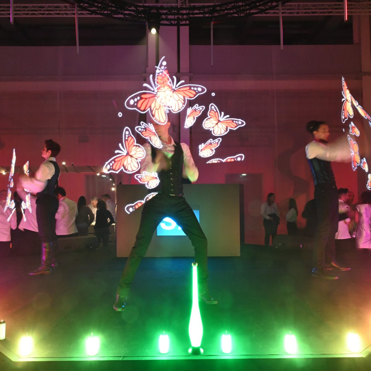 Trois artistes sur scène qui manipule des objets LED (lumineux) qui affichent des papillons et avec beaucoup de petites lumières posées au sol