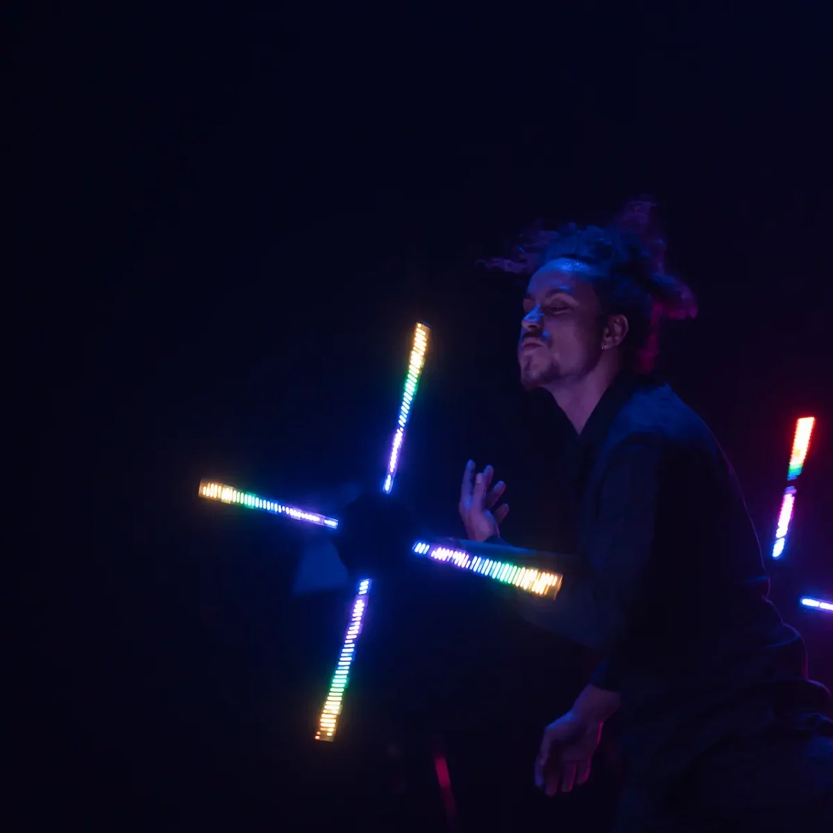 Un artiste sur scène crée des vagues de lumière bleues et blanches avec des objets LED en mouvement